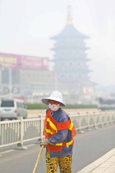 近日，在古都洛陽，環(huán)衛(wèi)工人身后的“天堂”被霧霾籠罩著。
