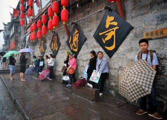 　4月29日上午11時20分，一些游客和古城當(dāng)?shù)氐木用穸阍谝粋€酒吧的屋檐下避雨。這些當(dāng)?shù)鼐用褚詾橛慰团恼罩\生，一場降雨讓他們的生意更加清淡。