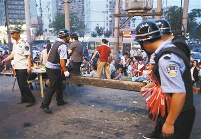 6月13日晚8點(diǎn)，朝陽(yáng)路和青年路交叉口西側(cè)，一次聯(lián)合執(zhí)法行動(dòng)中，輔警與協(xié)管抬走商戶(hù)的燒烤用具。新京報(bào)記者 尹亞飛 攝