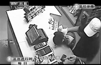 戴帽男子一手掐住加油站營業(yè)員，一手持發(fā)令槍指向另一營業(yè)員，要求“把錢給我裝起來”。