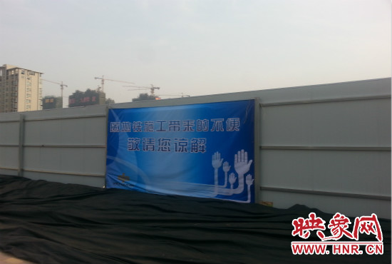 道路南側圍起了白色的圍擋，墻上標示著“因地鐵施工帶來的不便敬請您諒解”的提示牌。