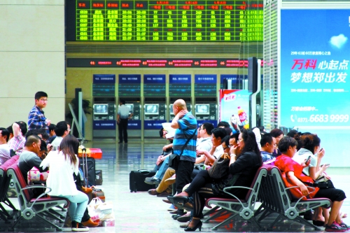 候車大廳溫度很高，一名乘客一手扇風(fēng)、一手擦汗