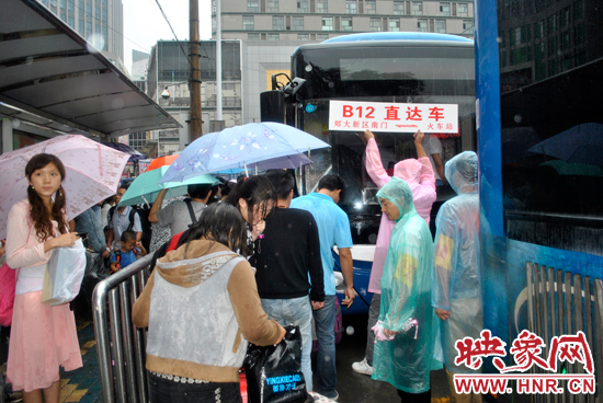 公交志愿者雨中高舉“B12-直達車”指示牌疏導返校學生乘車 公交志愿者雨中高舉“B12-直達車”指示牌疏導返校學生乘車
