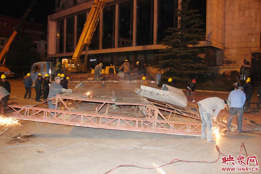 地面上的20多名工人對吊裝下的廣告牌進行分割。