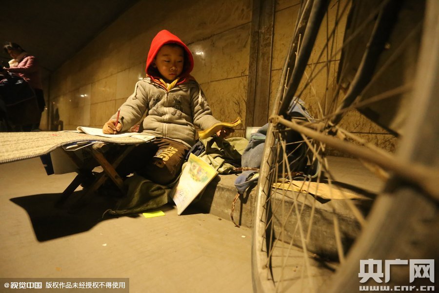 2015年11月8日晚，鄭州，7歲男孩涵洞橋下陪父母練攤，路邊燈下坐小馬扎上寫作業(yè)。