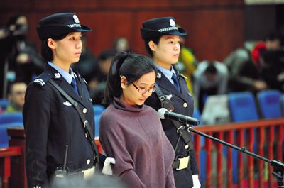 被告人盧梅低著頭，站在朝陽法院刑事審判庭的被告席上。