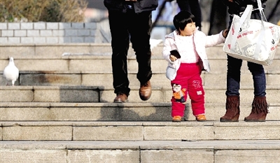 昨天中午，一女孩拉著家長(zhǎng)的手在紫荊山公園曬太陽，氣溫升高，孩子的棉衣解開了扣子。