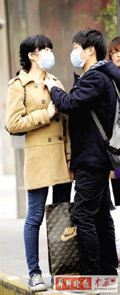 公交站臺(tái)上，一對(duì)年輕人戴著口罩，系緊衣領(lǐng)。